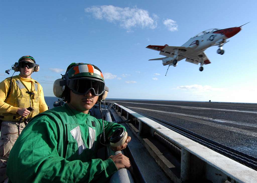 A deck edge operator and arresting gear officer ensure the flight deck is  clear for an incoming T-45C Goshawk training jet aboard the aircraft  carrier USS John F. Kennedy (CV 67). 